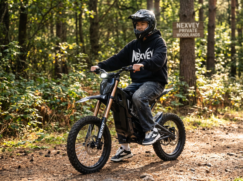 A helmeted rider on a black NEXVEY FLASH 2 electric dirt bike in sunlit woodland