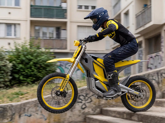 A rider in professional gear catching air on a yellow NEXVEY FLASH electric dirt bike while jumping down concrete stairs in a city setting