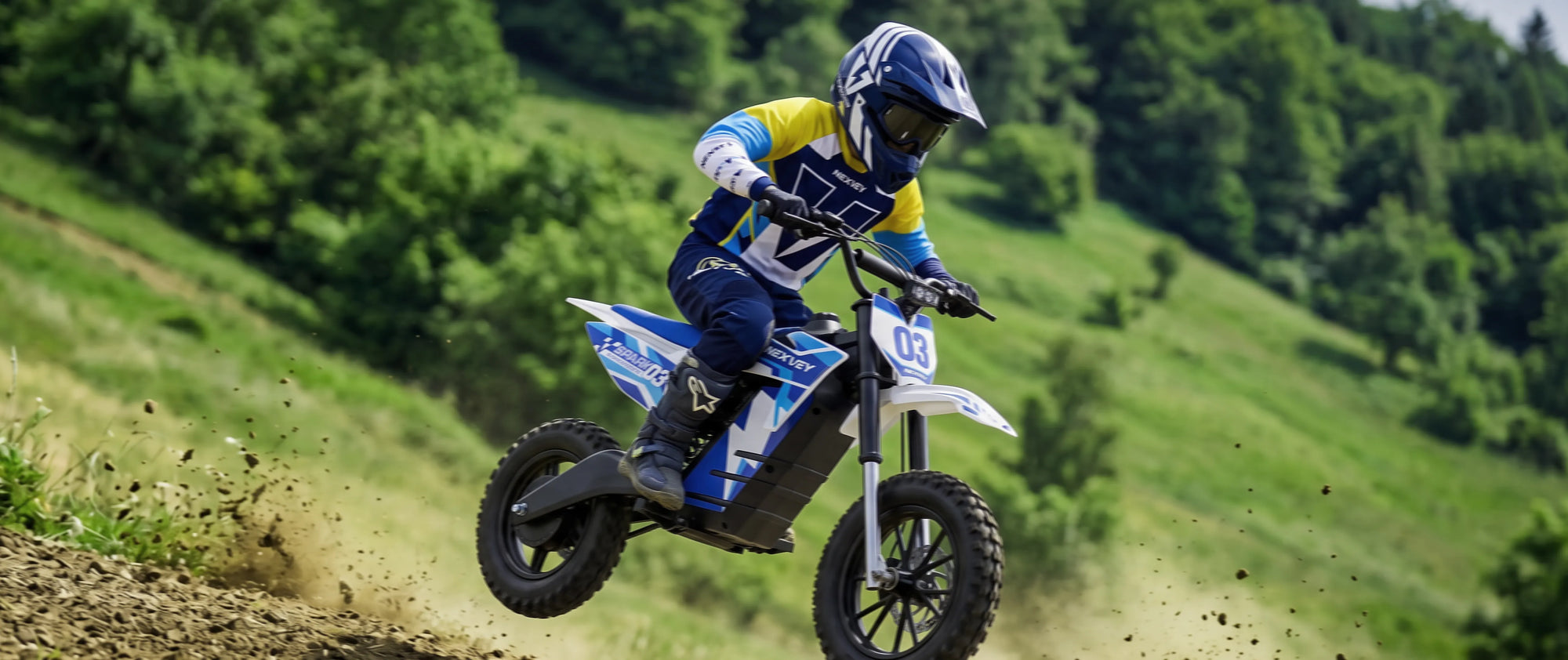 A young rider jumping a NEXVEY SPARK series electric dirt bike on a dirt track, showcasing the bike's blue and white lightning bolt graphics and off-road suspension.