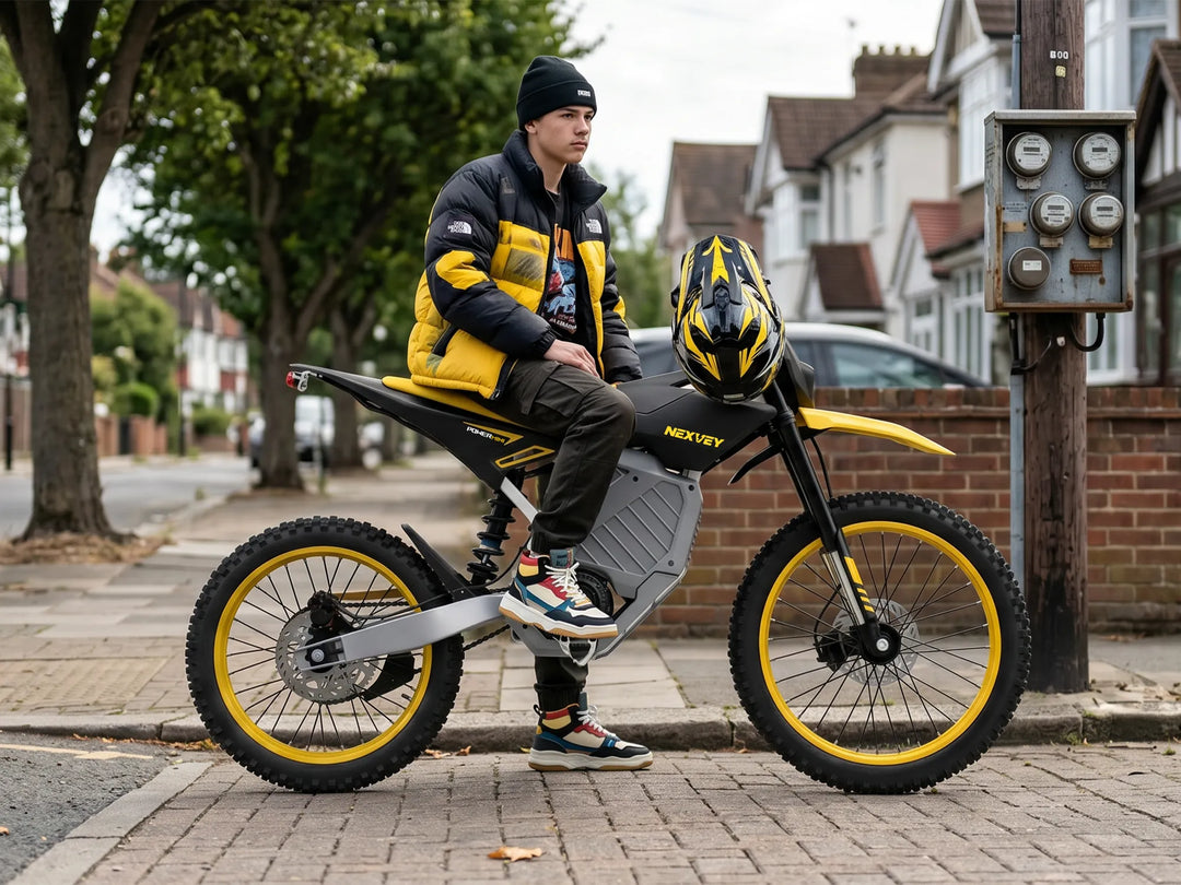 A young rider wearing a beanie and yellow jacket sitting on a yellow and black NEXVEY STORM Electric Dirt Bike beside a residential sidewalk, with a helmet on the handlebars.