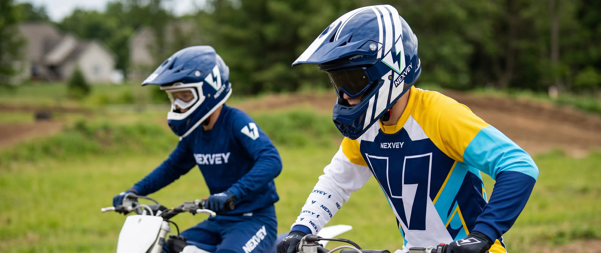 Close-up of a NEXVEY youth electric dirt bike helmet in dark blue and yellow, part of a full-face riding gear set, on a teen rider at a track with a second rider in the background.