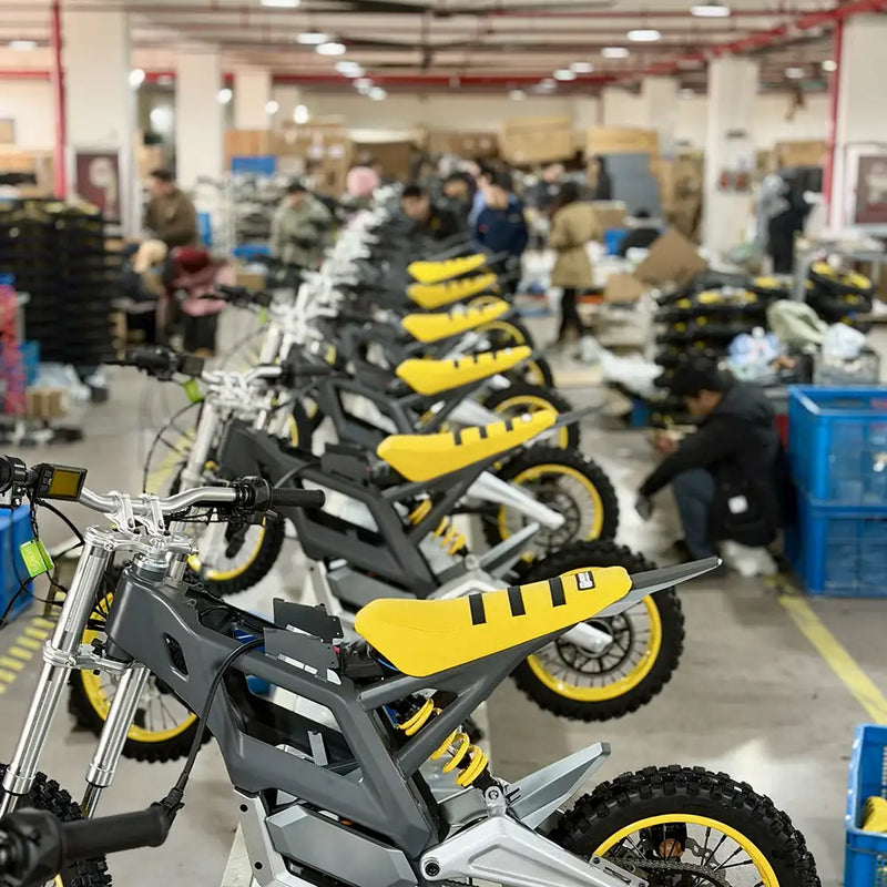 A long row of NEXVEY electric motocross bikes in a factory assembly line, showcasing high-volume manufacturing of grey and yellow off-road e-bikes.