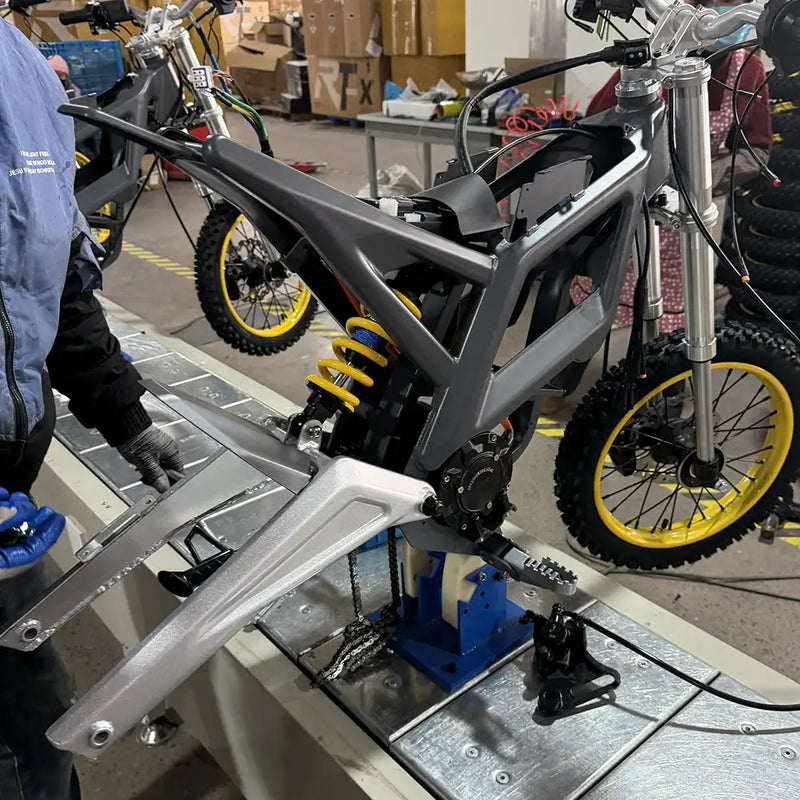 Close-up of the assembly line for NEXVEY electric dirt bikes, showing the high-quality frame, yellow rear shock absorber, and motor installation