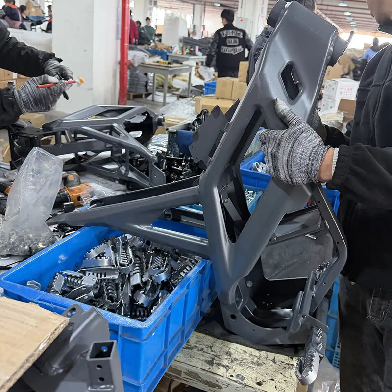 A worker inspecting a durable grey NEXVEY electric dirt bike frame on the production line with bins of metal footpegs