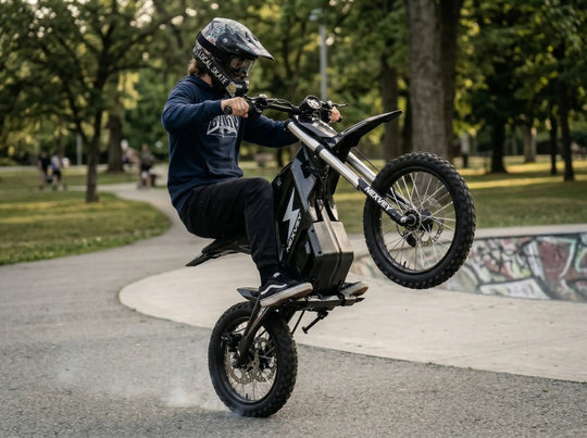 A rider in a blue hoodie and sticker-covered helmet performing a powerful wheelie on a black NEXVEY FLASH electric dirt bike with tire smoke at a graffiti skatepark