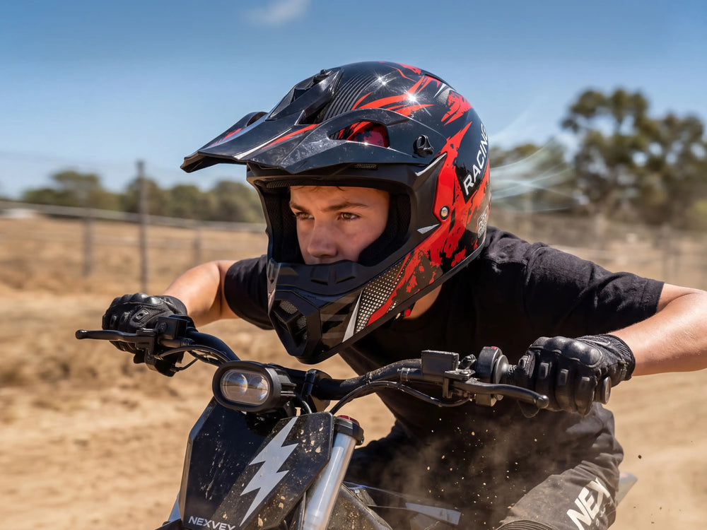 A young rider wearing a black and red NEXVEN motocross helmet and racing gloves, riding a black electric dirt bike with a lightning bolt logo on a dusty outdoor track
