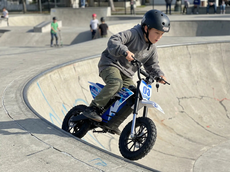 A young boy riding a NEXVEY Spark D3 electric dirt bike along the edge of a concrete bowl at a skatepark