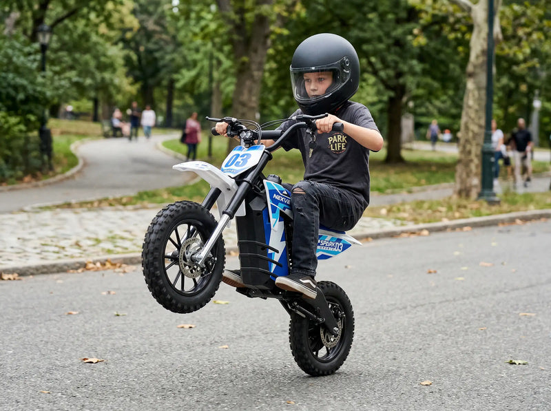 A young boy performing a wheelie on a NEXVEY Spark D3 blue electric dirt bike in an outdoor park setting