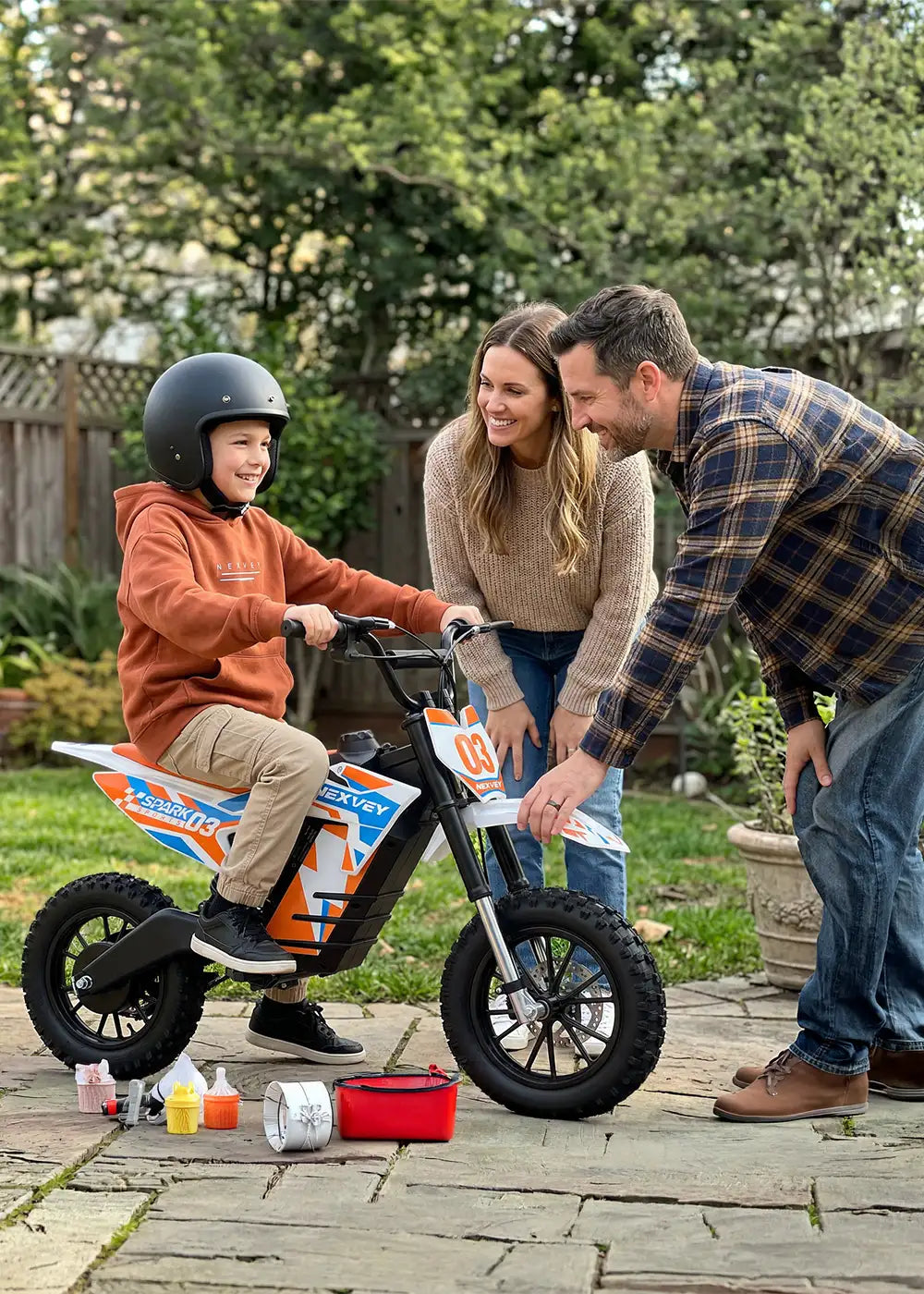 Happy parents gifting a NEXVEY Spark D3 orange electric dirt bike to their son in a backyard setting
