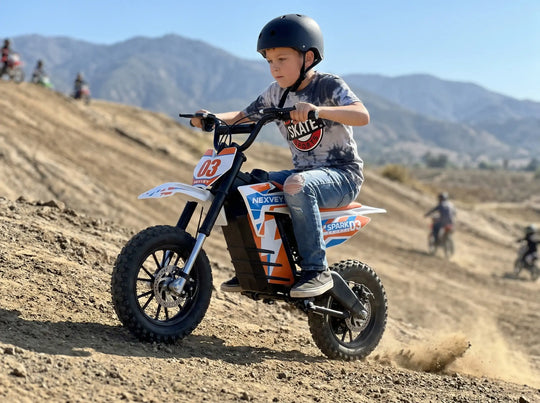A young boy in a helmet riding an orange and white NEXVEY SPARK 03 electric dirt bike on a rugged mountain trail, kicking up dust for an outdoor adventure