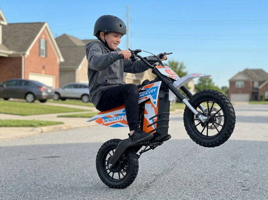 A young boy in a black helmet performing a wheelie on an orange and white NEXVEY SPARK 03 electric dirt bike on a suburban neighborhood street