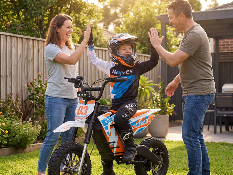 A young boy on an orange and white NEXVEY Spark 03 kids electric dirt bike giving high-fives to his parents in a backyard, wearing a full-face motocross helmet for safety