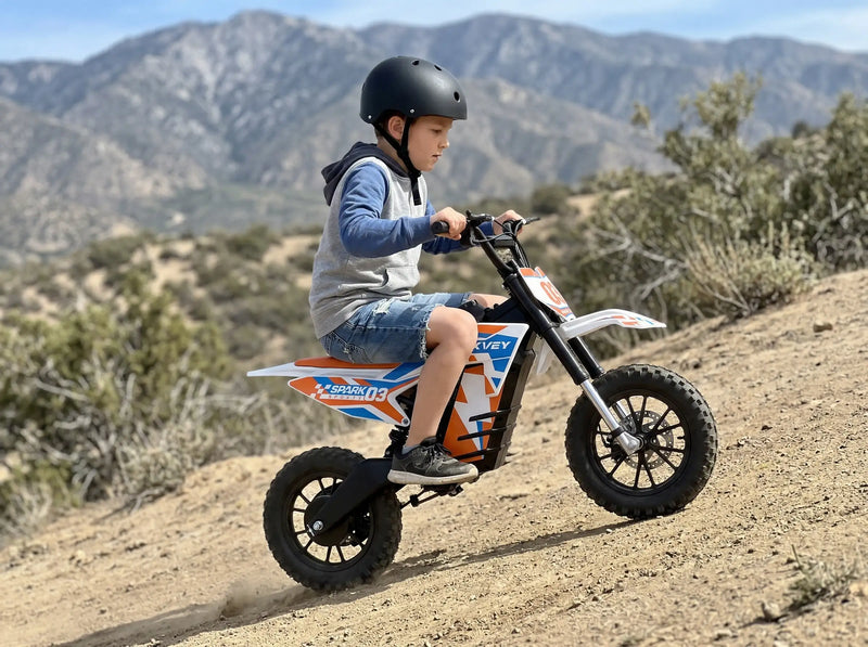 Teenager riding a white and orange NEXVEY "Spark 03" electric dirt bike for kids on a mountain trail, wearing a black safety helmet