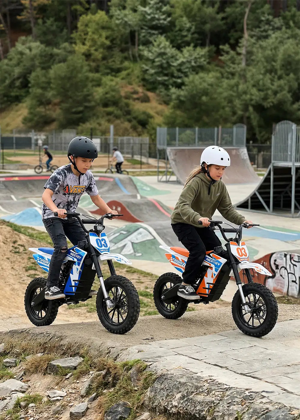 Two children wearing safety helmets riding NEXVEY electric dirt bikes at a skate park pump track