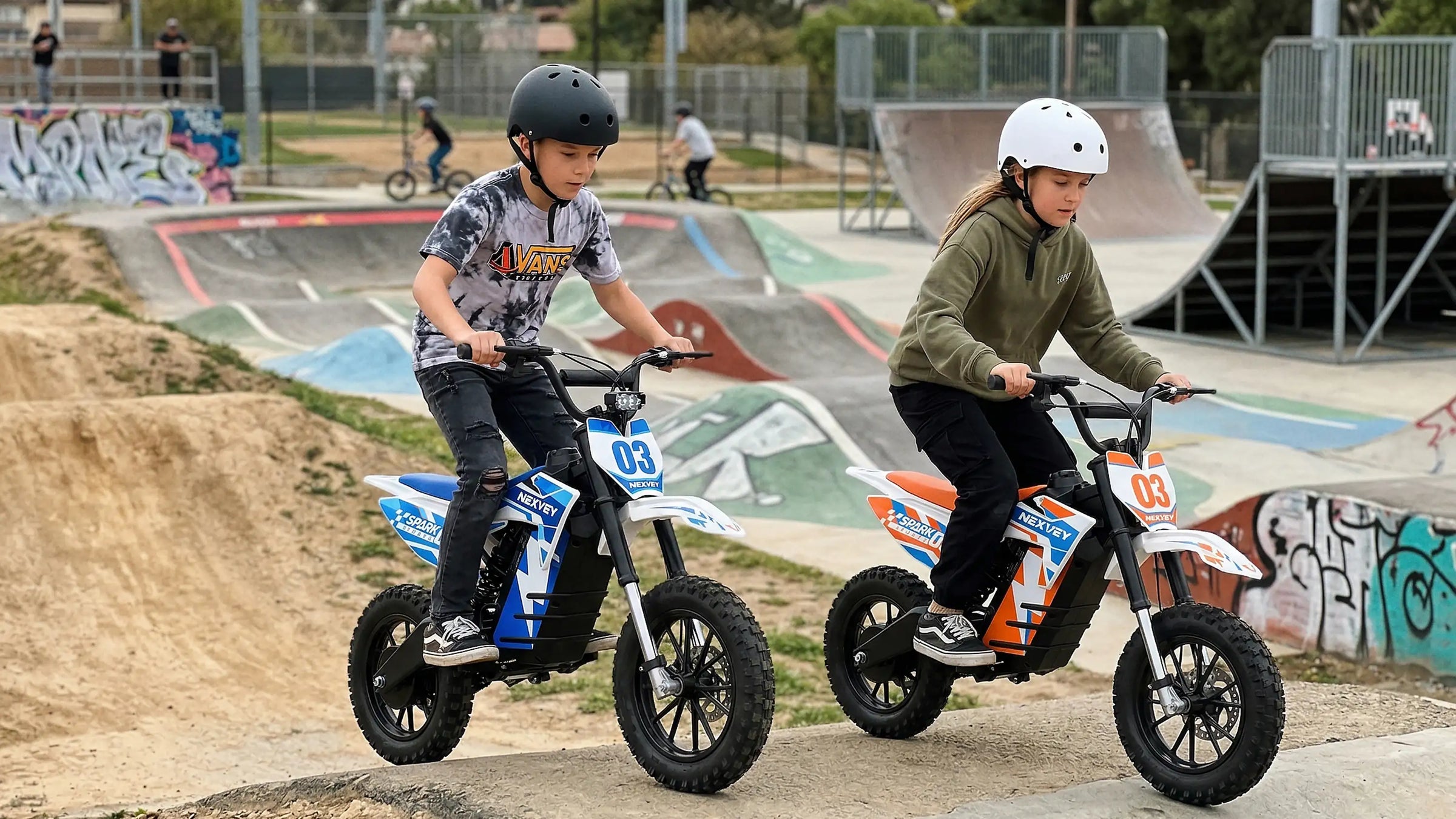 Two kids wearing protective helmets riding NEXVEY electric mini dirt bikes on a concrete pump track at a skate park